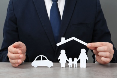 Photo of Man with cutout paper family, house roof and car at table, closeup. Life insurance concept