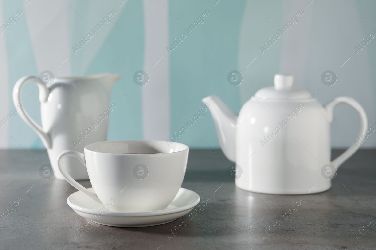 Photo of Aromatic tea in teapot, cup and pitcher on gray table against color background