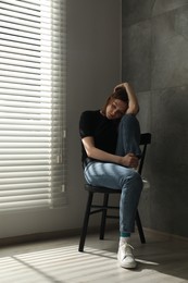 Photo of Sad young woman sitting on chair at home