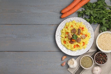 Photo of Delicious pilaf with meat and ingredients on grey wooden table, flat lay. Space for text