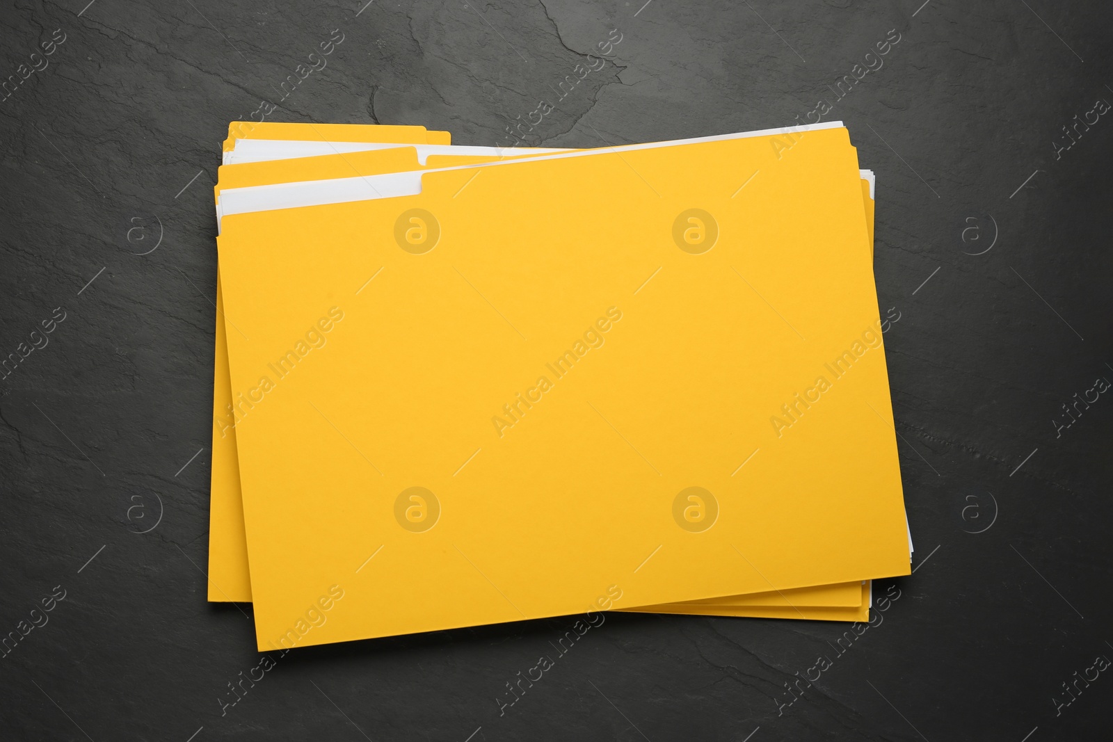 Photo of Yellow files with documents on black slate table, top view