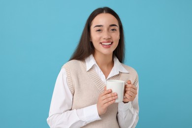 Photo of Happy young woman holding white ceramic mug on light blue background