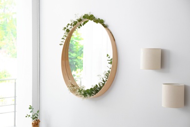 Photo of Round mirror with green branches on white wall in modern room interior