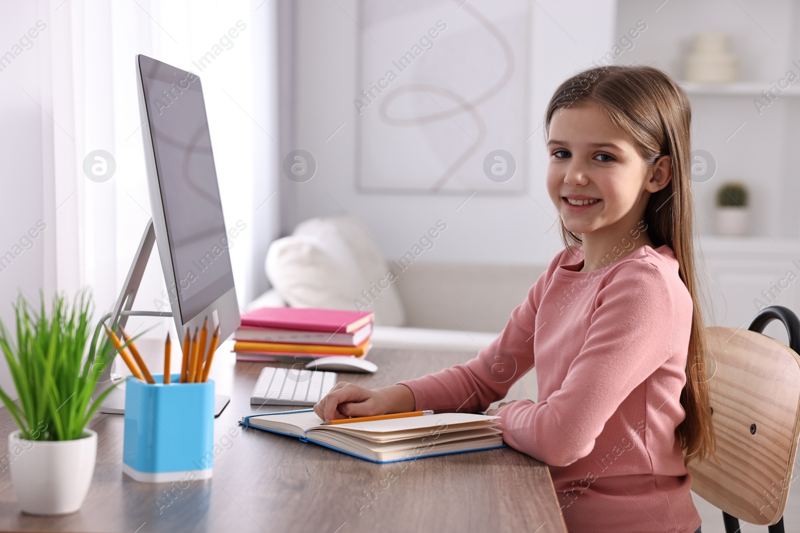 Photo of E-learning. Cute girl using computer during online lesson at table indoors