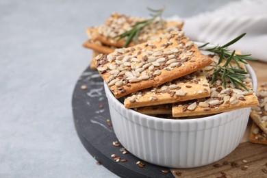 Photo of Cereal crackers with flax, sunflower, sesame seeds and rosemary in bowl on grey table, closeup. Space for text