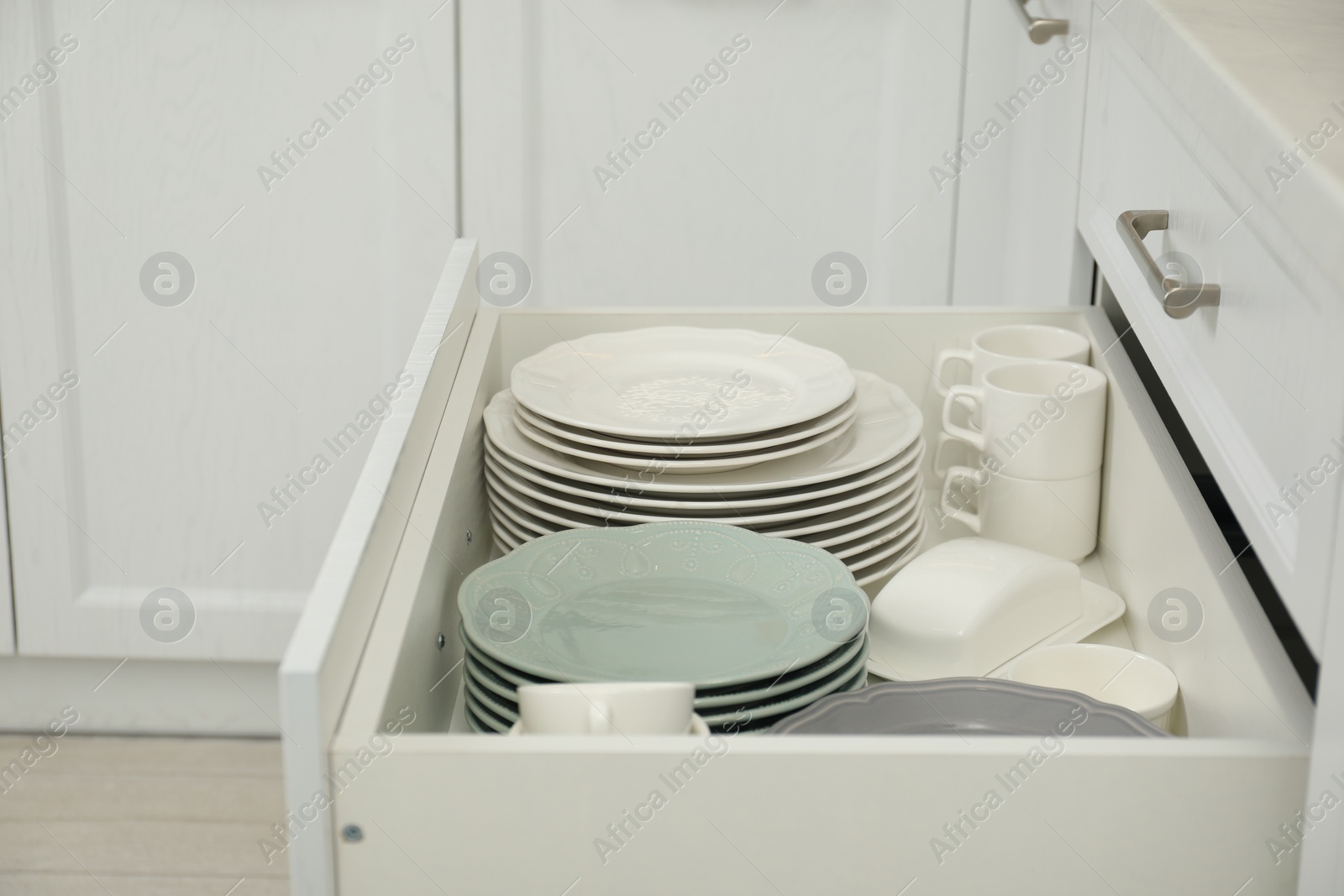 Photo of Clean plates, cups and butter dish in drawer indoors