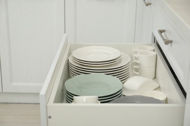 Photo of Clean plates, cups and butter dish in drawer indoors