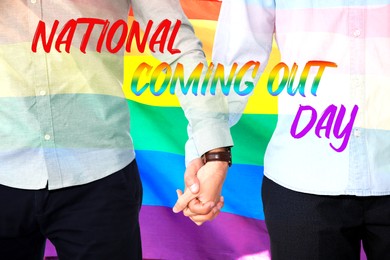 Image of National Coming Out day. Gay couple holding hands against rainbow pride flag, closeup