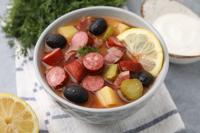 Photo of Meat solyanka soup with thin dry smoked sausages in bowl on grey table, closeup