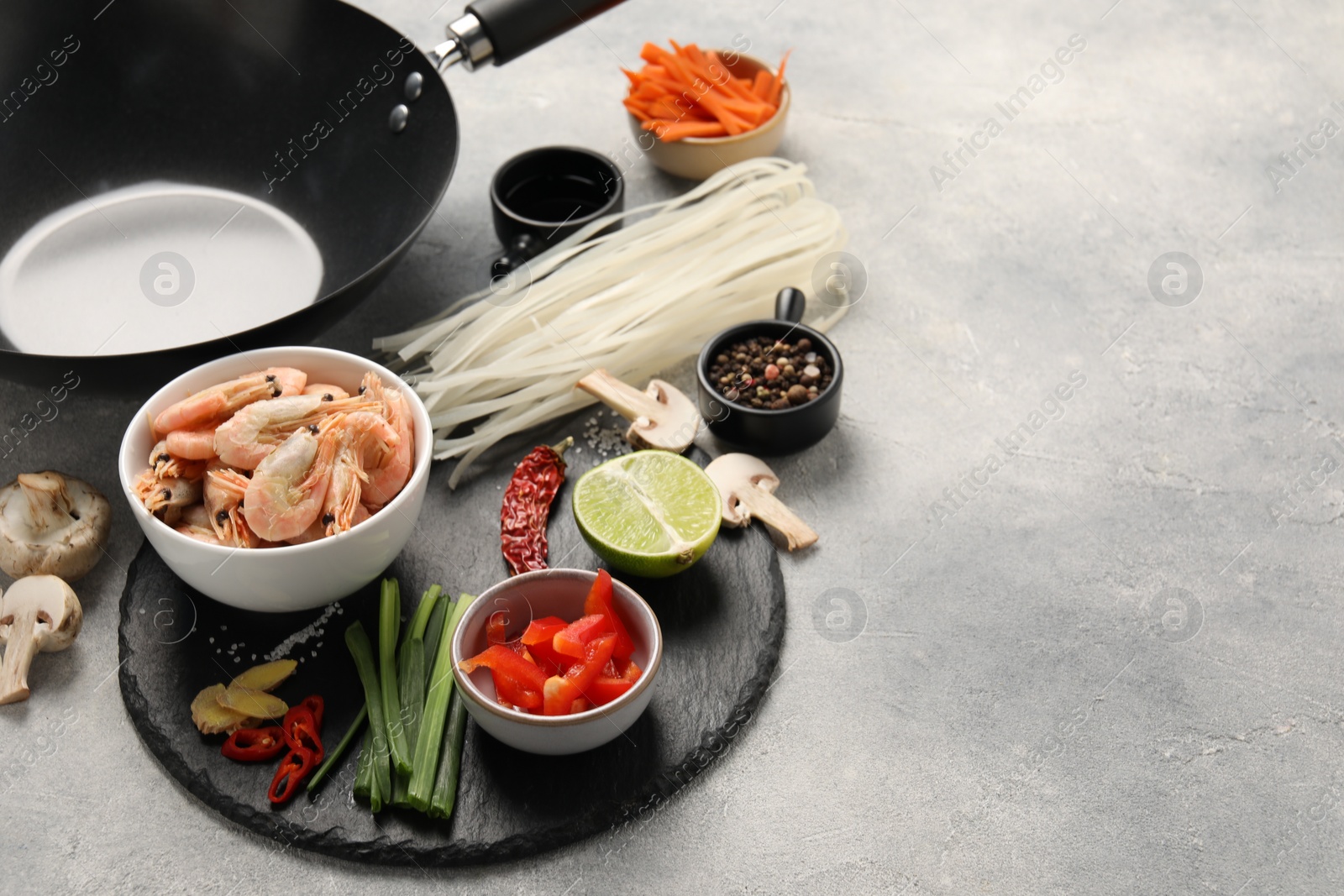 Photo of Different products and black wok on grey table, closeup. Space for text