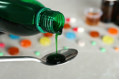 Photo of Pouring cough syrup into spoon against blurred background, closeup