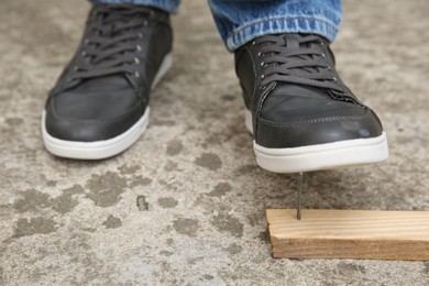 Careless man stepping on nail in wooden plank outdoors, closeup