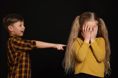 Photo of Boy laughing and pointing at upset girl on black background. Children's bullying