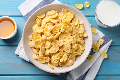 Photo of Tasty crispy corn flakes served with milk and honey on light blue wooden table, flat lay