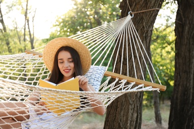 Photo of Young woman reading book in comfortable hammock at green garden