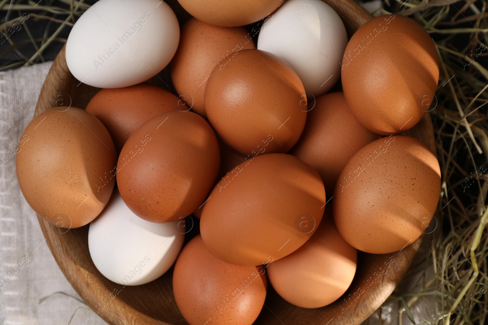 Photo of Fresh chicken eggs in bowl and dried hay on table, flat lay