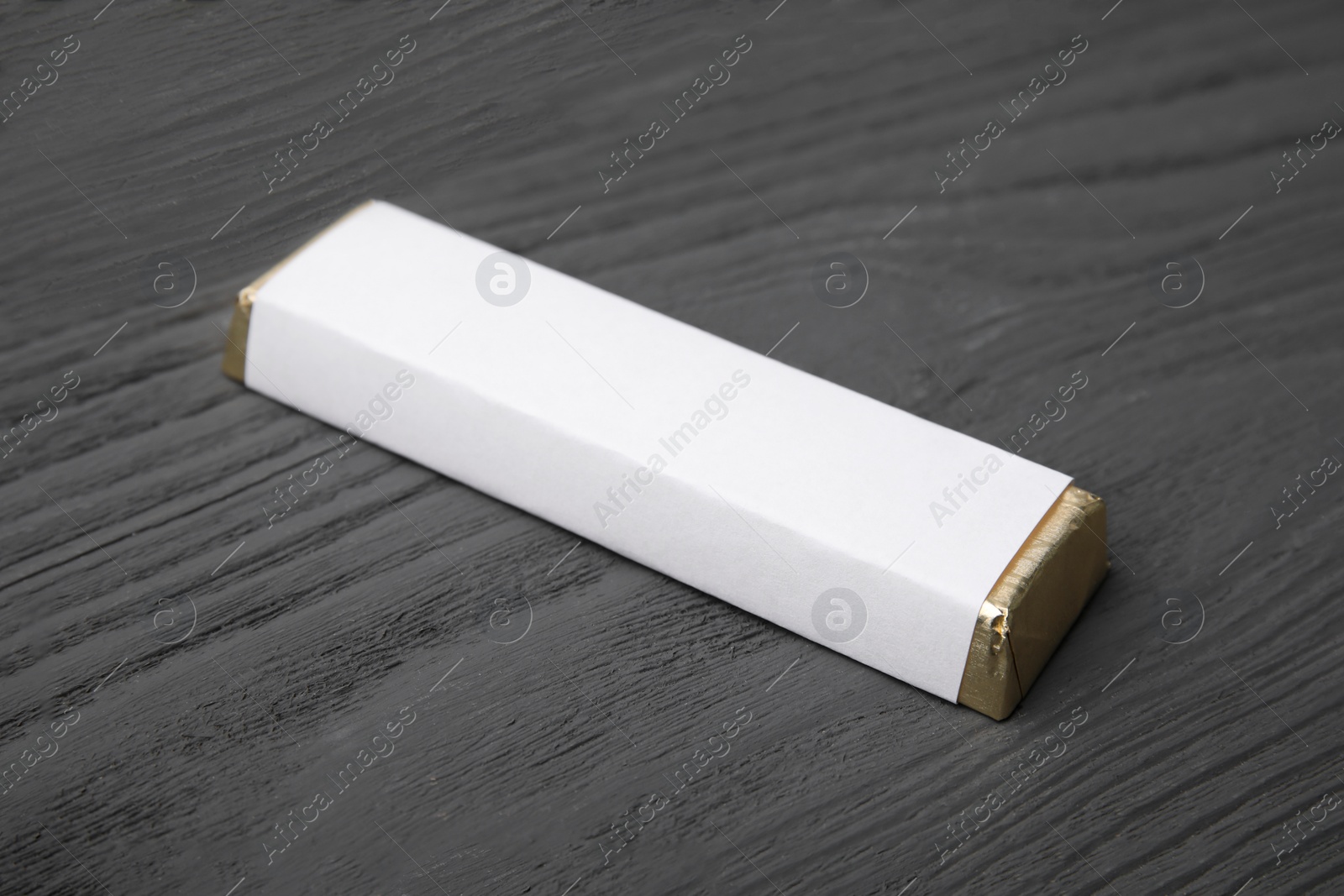 Photo of Tasty chocolate bar in package on grey wooden table, closeup