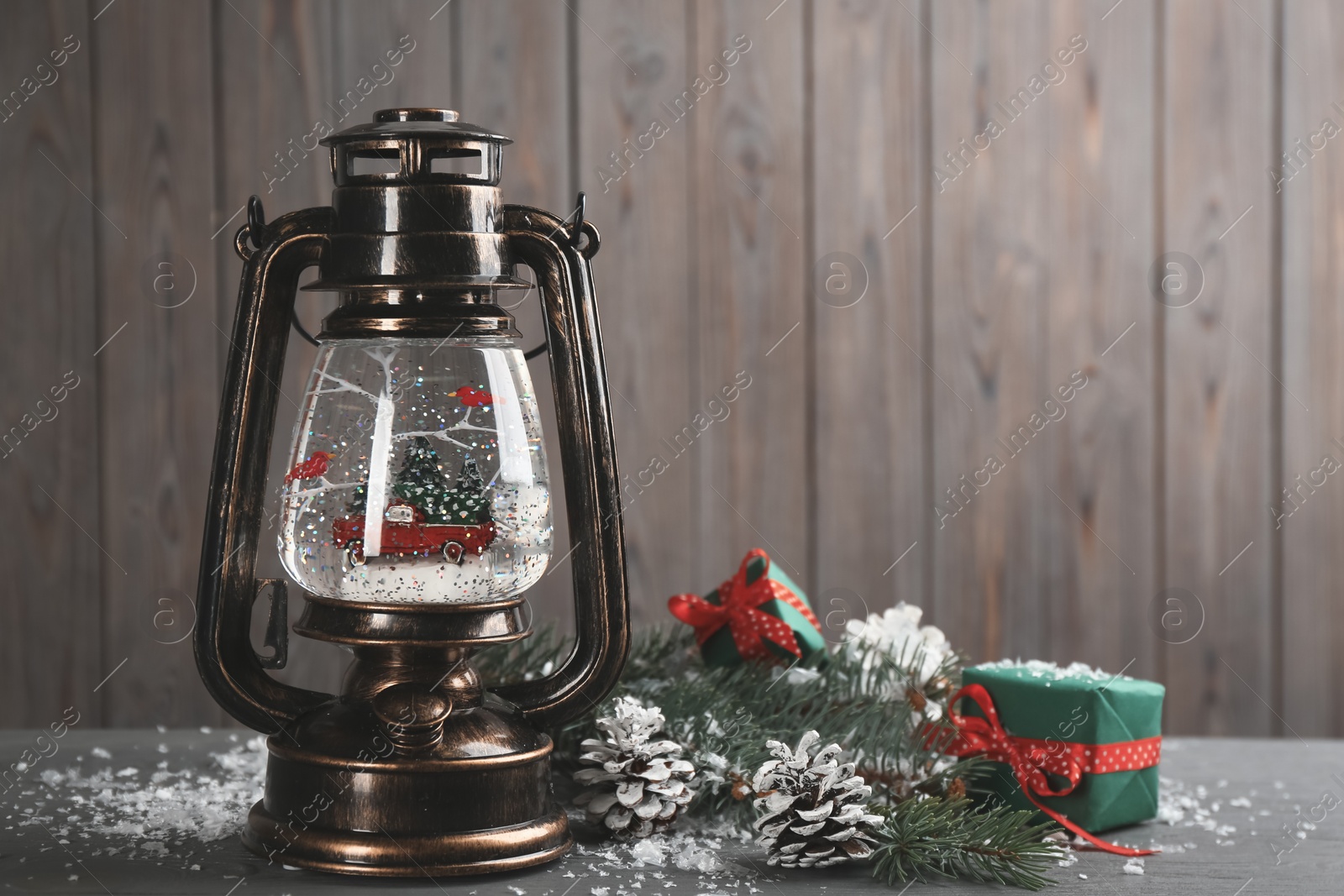 Photo of Beautiful snow globe in vintage lantern, gifts and Christmas decor on grey wooden table. Space for text