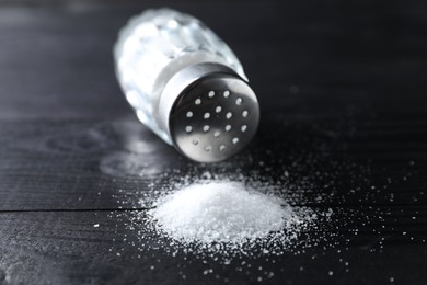 Photo of Organic salt in glass shaker on black wooden table, closeup