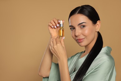 Young woman with bottle of essential oil on beige background. Space for text