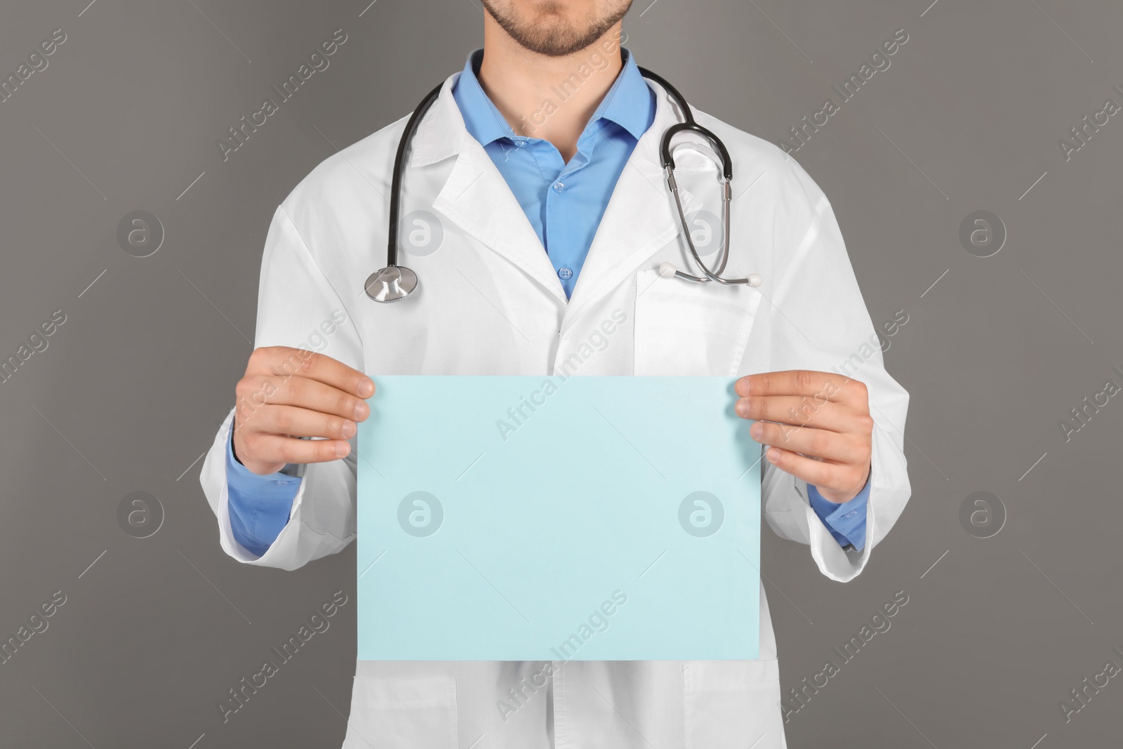 Photo of Male doctor holding blank sheet of paper on grey background