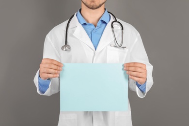 Male doctor holding blank sheet of paper on grey background