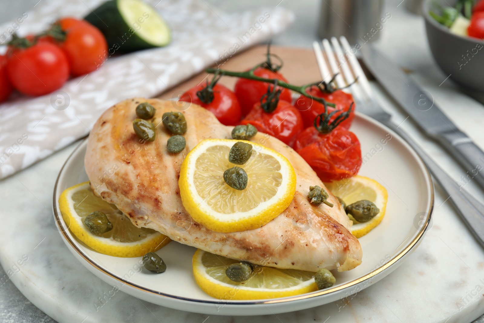 Photo of Delicious cooked chicken fillet with capers, tomatoes and lemon on table, closeup