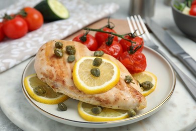 Photo of Delicious cooked chicken fillet with capers, tomatoes and lemon on table, closeup