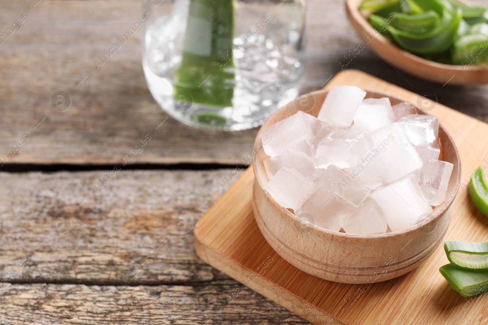 Photo of Aloe vera gel and slices of plant on wooden table, closeup. Space for text