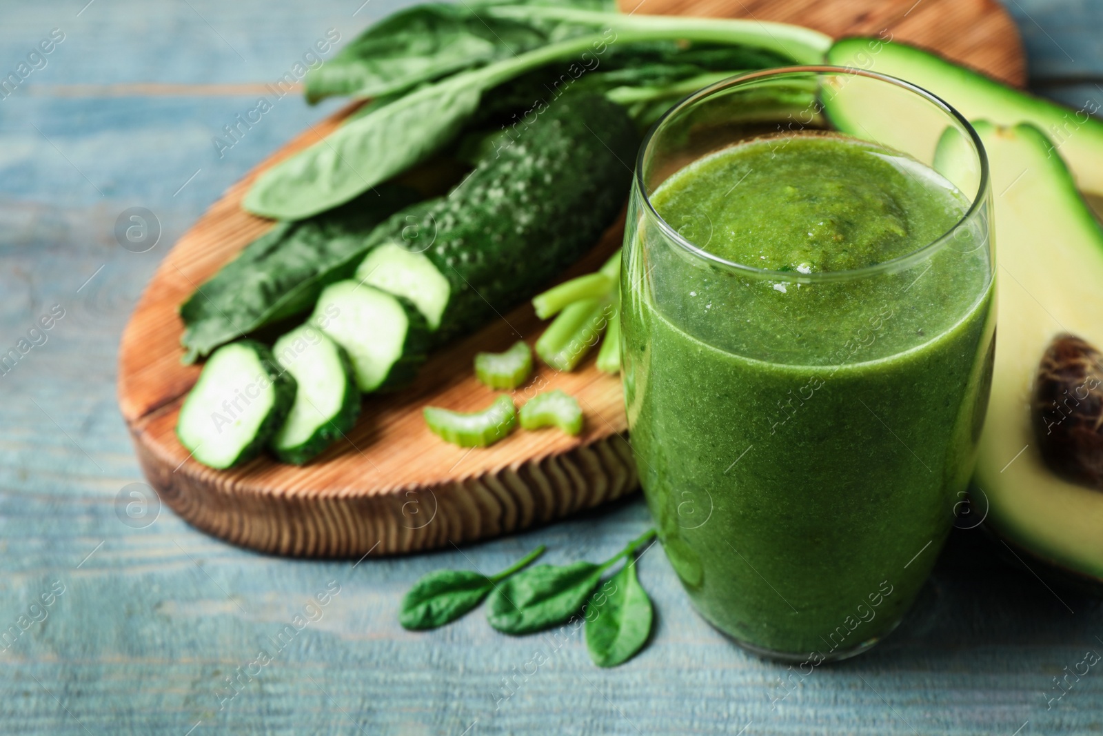 Photo of Delicious green juice and fresh ingredients on light blue wooden table, closeup. Space for text