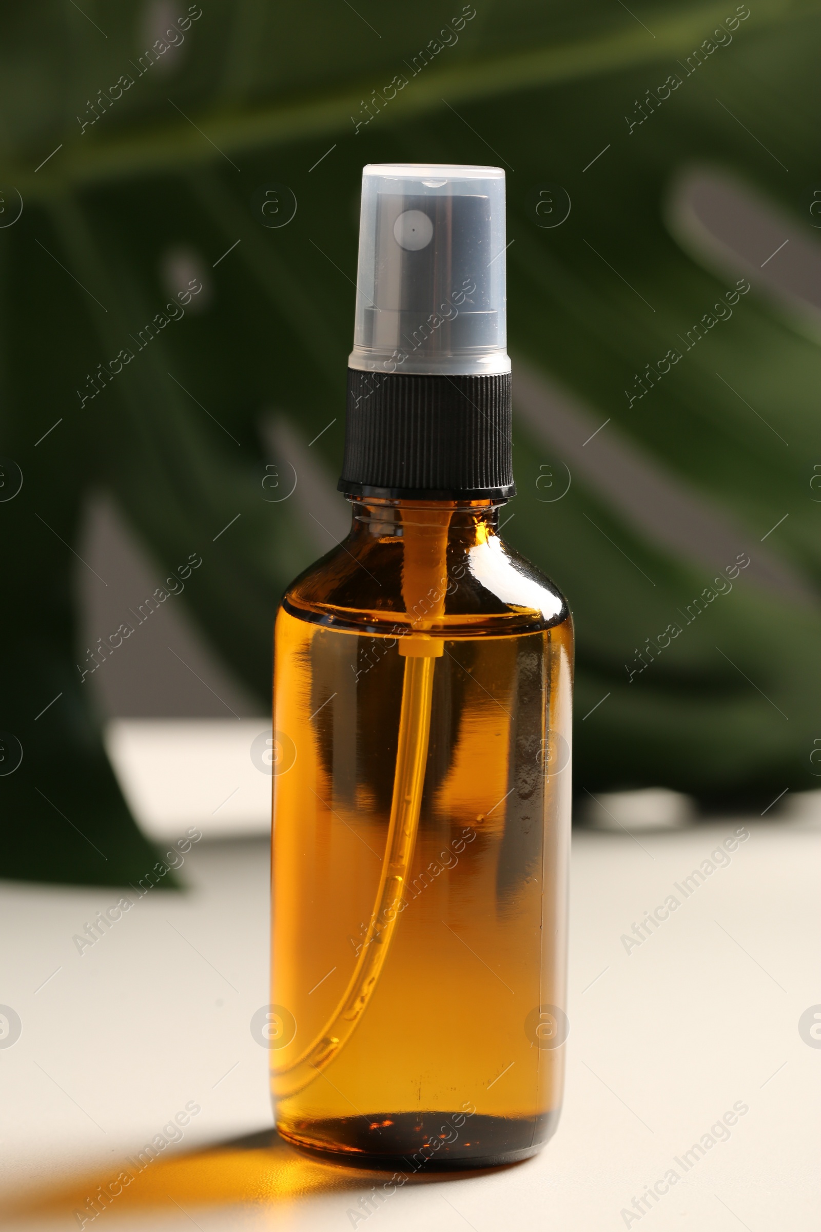Photo of Spray bottle with oil and green leaf on white table. Natural cosmetics