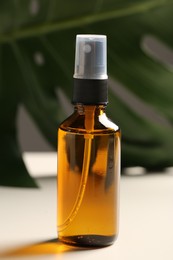 Photo of Spray bottle with oil and green leaf on white table. Natural cosmetics