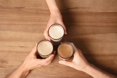 Photo of People holding glasses with protein shakes on wooden background, above view