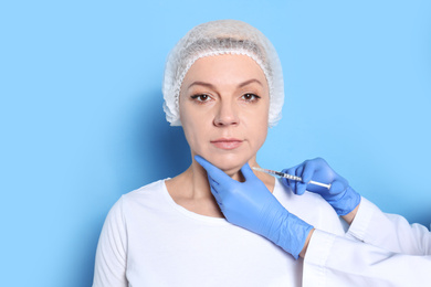 Mature woman with double chin receiving injection on blue background