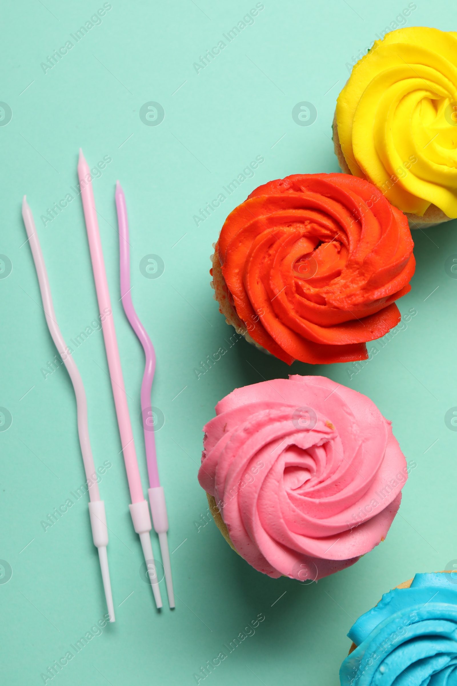 Photo of Delicious cupcakes with bright cream and candles on turquoise background, flat lay