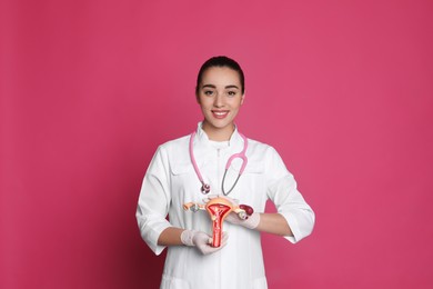 Photo of Doctor demonstrating model of female reproductive system on pink background. Gynecological care