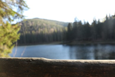 Lake near mountain forest on sunny day, focus on wooden fence