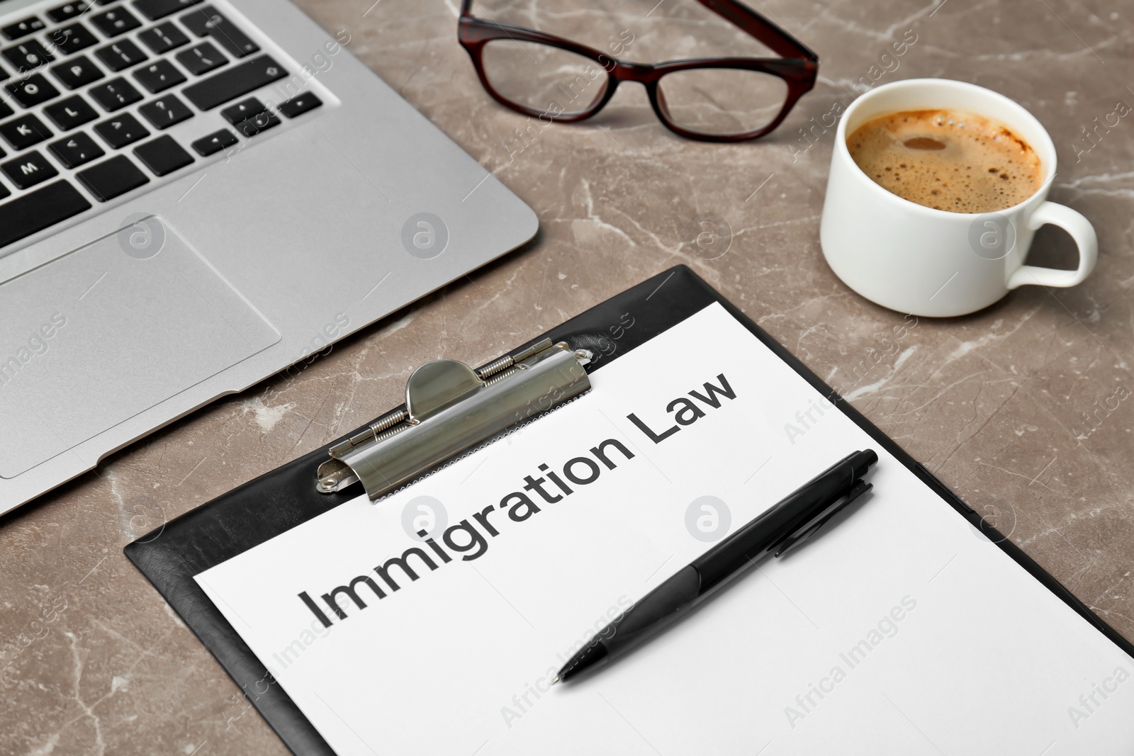 Photo of Clipboard with words IMMIGRATION LAW, laptop and coffee on table, closeup