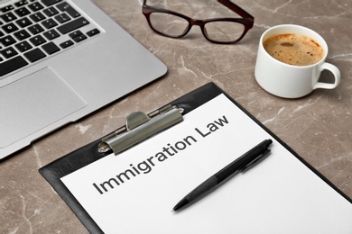 Clipboard with words IMMIGRATION LAW, laptop and coffee on table, closeup