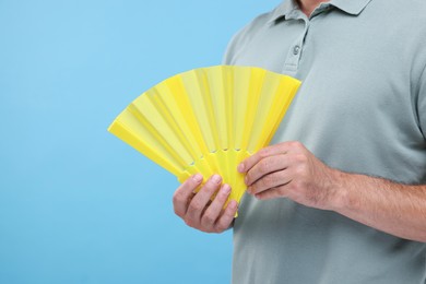 Photo of Man holding hand fan on light blue background, closeup. Space for text