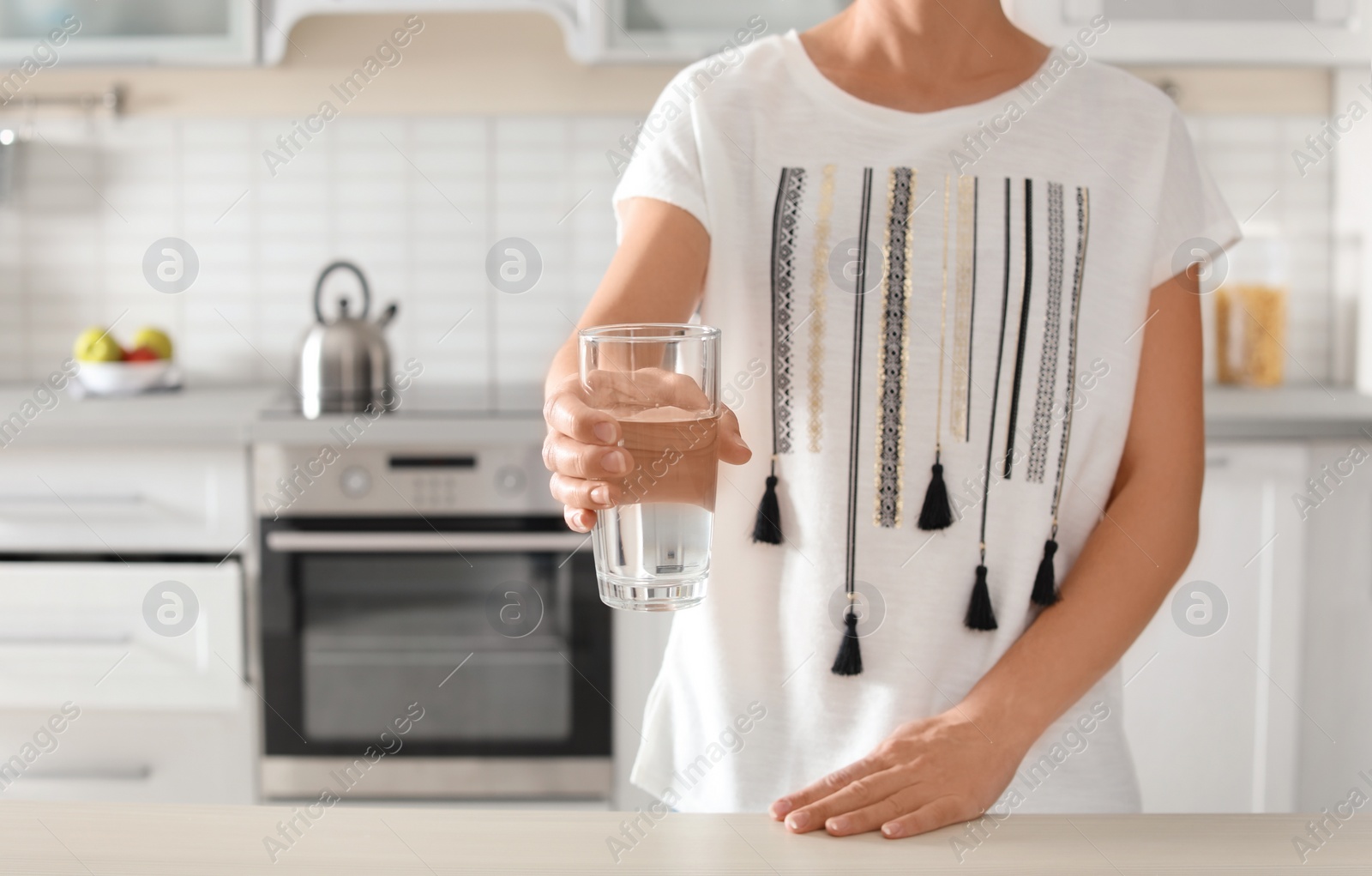 Photo of Woman holding glass with clean water in kitchen, closeup. Space for text