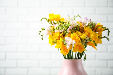 Photo of Beautiful blooming freesias in vase against white brick wall. Space for text