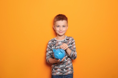 Photo of Little boy putting coin into piggy bank on color background