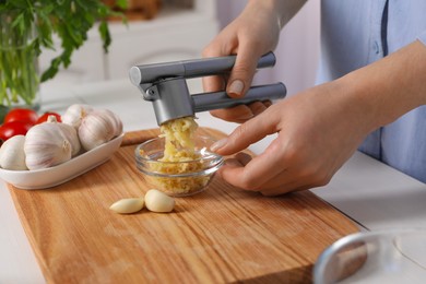 Photo of Woman squeezing garlic with press at white wooden table, closeup