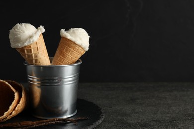 Photo of Ice cream scoops in wafer cones on gray textured table against dark background, space for text