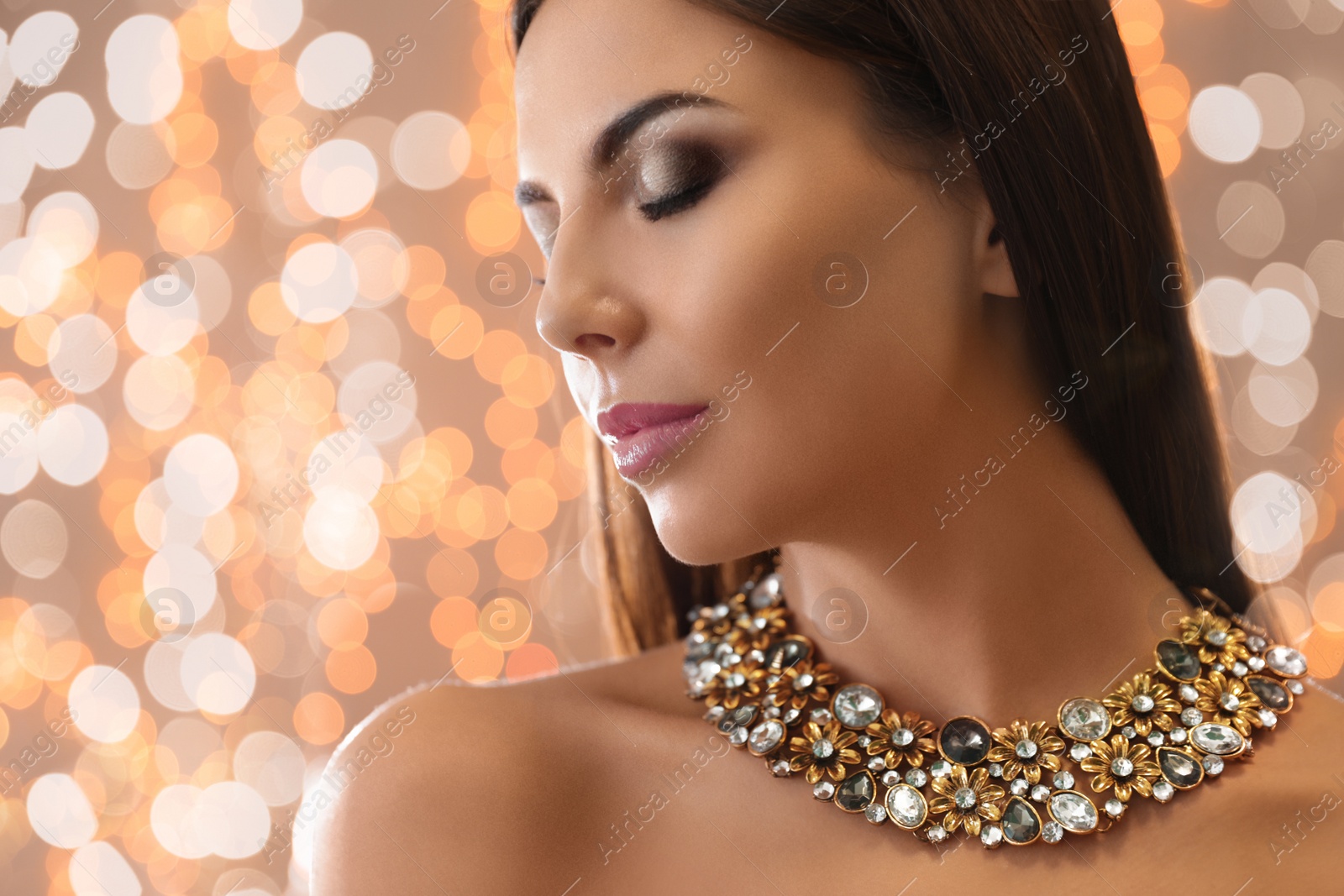 Photo of Beautiful young woman with elegant jewelry against defocused lights. Space for text