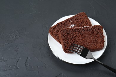 Photo of Pieces of tasty chocolate sponge cake with powdered sugar on black textured table. Space for text