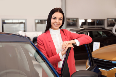 Young saleswoman near new car in dealership