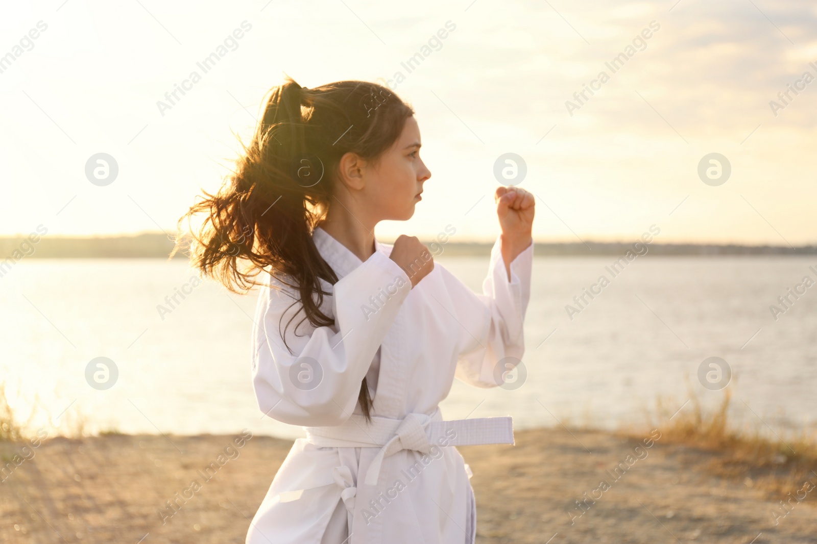 Photo of Cute little girl in kimono practicing karate near river on sunny day