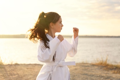 Cute little girl in kimono practicing karate near river on sunny day